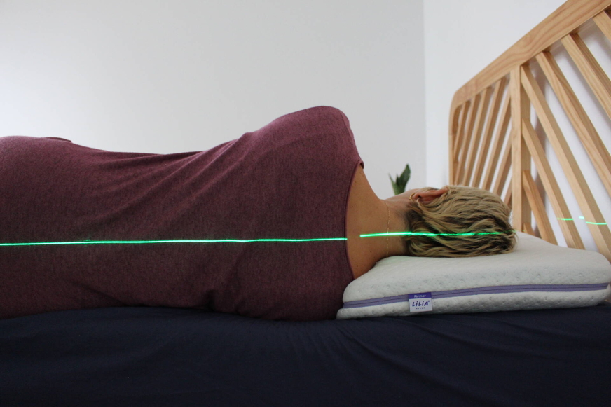 Pessoa de cabelo claro de costas para a câmara, deitada de lado numa almofada com um laser verde para mostrar o alinhamento da coluna.